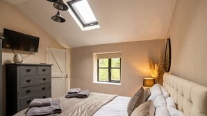 A bedroom with a bed, a dresser, a television, a window, and a skylight. - Tranquil cottage stay with fireplace and pond (Oswestry)