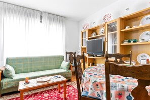 Una sala de estar con un sofá, una mesa de centro, un televisor y una estantería con platos decorativos.