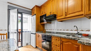 A kitchen with wooden cabinets, a granite countertop, a stainless steel sink, a microwave, an oven, and a sliding glass door leading to a balcony. - Apartment 'Carmina El Fondon 3' with Balcony and Wi-Fi (Cangas de Onís)