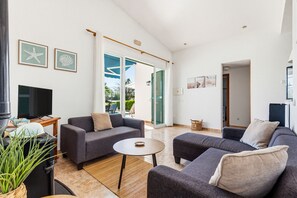 Ein Wohnzimmer mit einer Couch, einem Couchtisch, einem Fernseher und einer Pflanze.