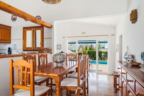 Ein Essbereich mit Holztisch und -stühlen, eine Küche mit Holzausstattung und Blick auf einen Swimmingpool durch Glastüren.