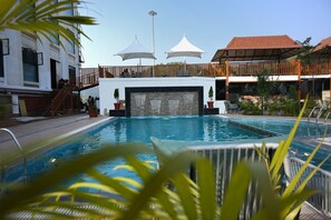 Una piscina con bordo in legno, ombrelloni e un edificio con balcone.