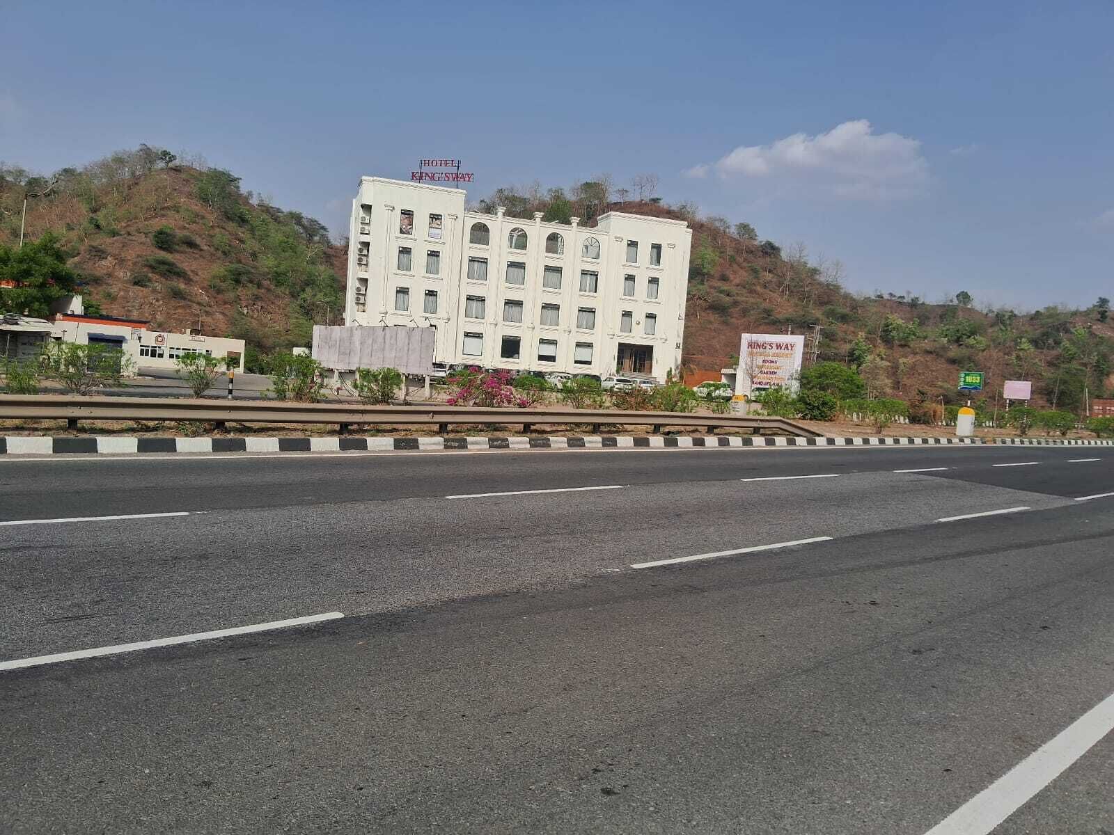 A multi-story hotel with a sign reading 'Hotel King Sway' on the roof, situated on a hillside with a clear road in the foreground.