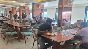 Un espace repas comprenant plusieurs tables et chaises, des ventilateurs de plafond et une vue dégagée grâce à de grandes fenêtres.