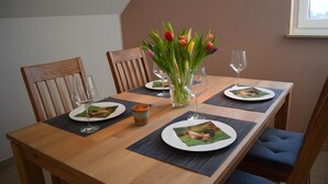 Ein Esstisch ist gedeckt mit Tellern, Gläsern und einer Blumenvase.