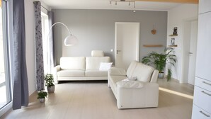 Ein modernes Wohnzimmer mit einer Couch, einem Sessel, einer Stehlampe und Topfpflanzen.