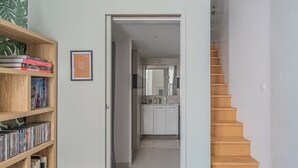 A modern interior with a wooden bookshelf, a framed picture, a small table, and a staircase leading to a kitchen area. - Nid du marché downtown La Rochelle, wifi (La Rochelle)
