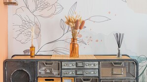 A vintage radio on a wooden table with a floral wall mural, a vase with dried flowers, and a wall-mounted light fixture. - Nid du marché downtown La Rochelle, wifi (La Rochelle)