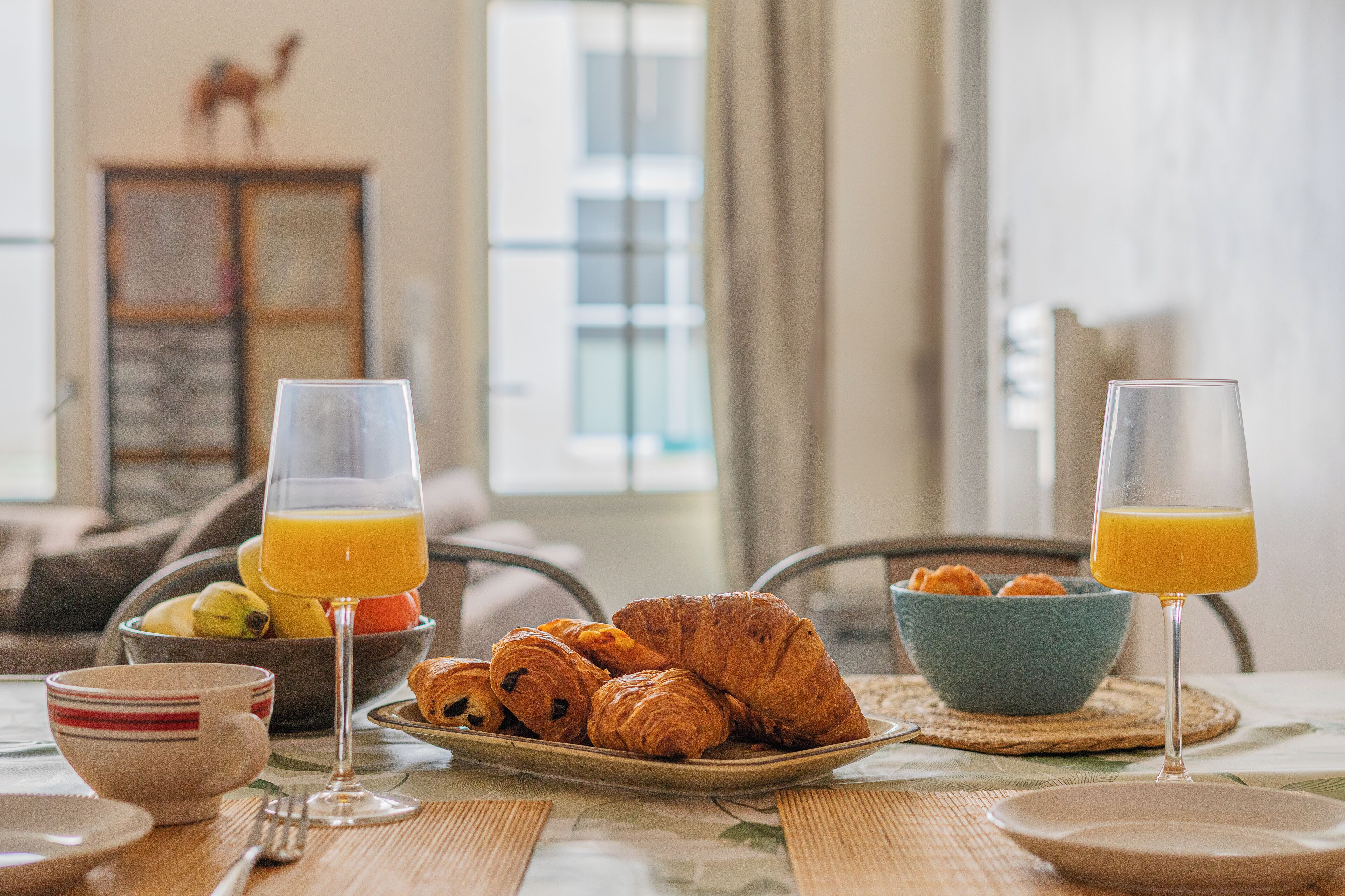 A breakfast setting with croissants, orange juice, and a bowl of fruit.