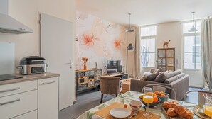 A modern kitchen with a microwave, a dining table set with breakfast, a sofa, and a TV in the background. - Nid du marché downtown La Rochelle, wifi (La Rochelle)