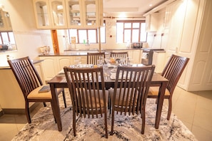 A dining area with a table set for six, surrounded by wooden chairs, in a kitchen with white cabinets and a window. - Border Point Apartments Westlands (Nairobi)