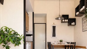 Een moderne woonkamer met een ronde tafel, een bank, een eethoek met stoelen, een keuken op de achtergrond en een potplant.