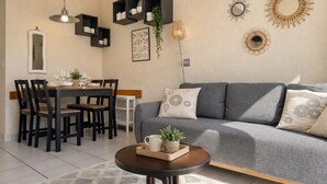 Een eetgedeelte met een tafel voor vier personen, een grijze bank met gestreepte kussens en wandplanken met decoratieve objecten.