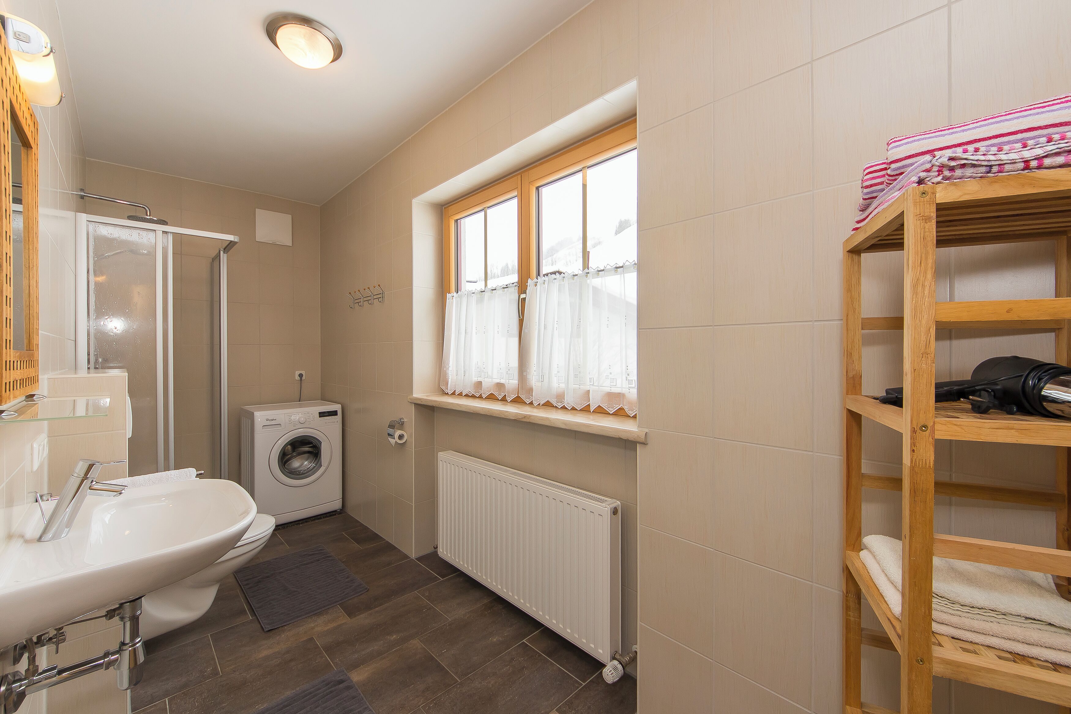 A bathroom with a shower, sink, toilet, and a window with curtains.