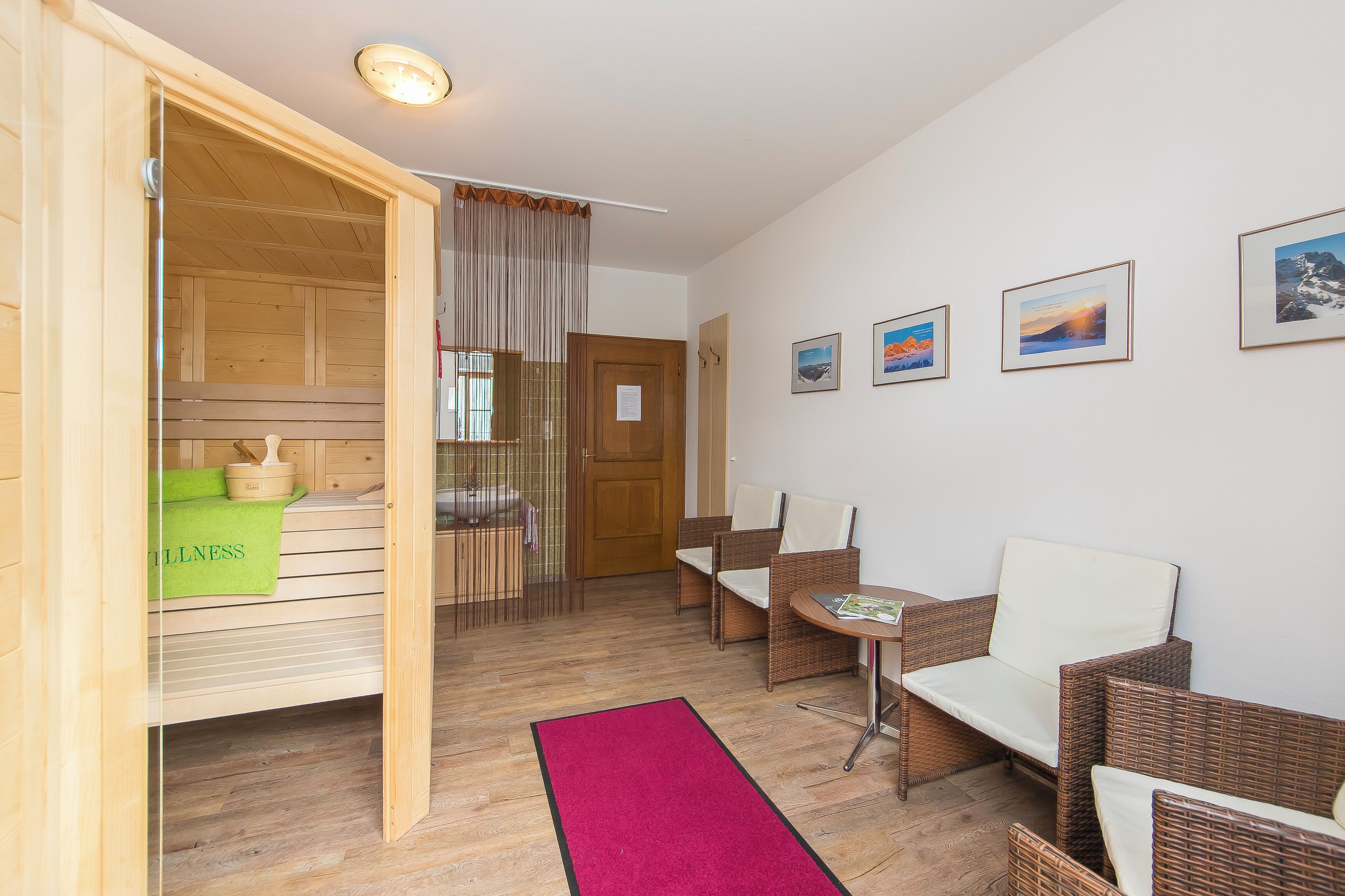 A room with a wooden sauna, wicker furniture, a red rug, and framed pictures on the wall.