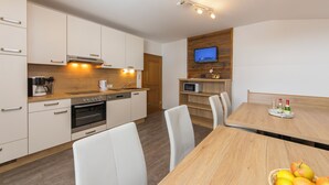 Una cocina moderna con gabinetes blancos, horno empotrado y zona de comedor con mesa y sillas de madera.