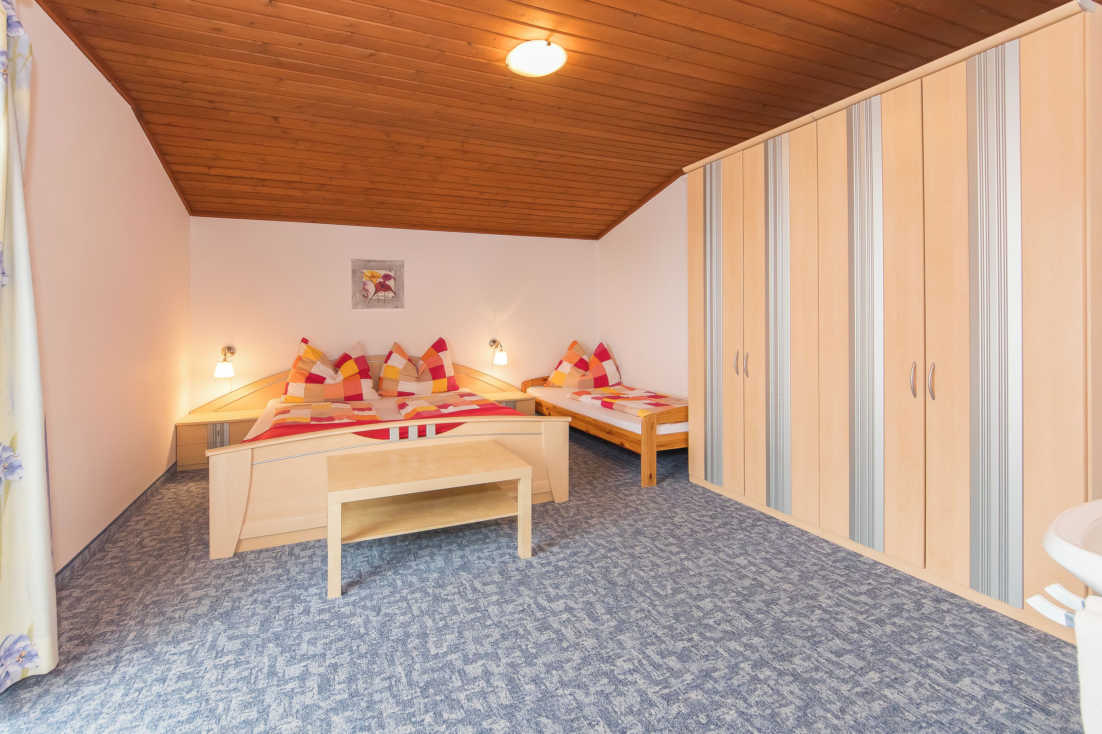 A bedroom with two single beds, a wooden bench, a wardrobe, and a small table.