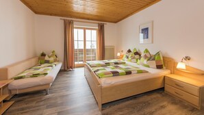 Una habitación con techo de madera, una cama con colcha, una mesita de noche con lámpara y una ventana con cortinas.