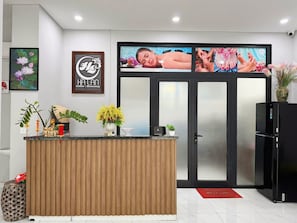 Un comptoir d’accueil avec un panneau en bois, un espace dédié au café et un écran fixé au mur diffusant une publicité pour des massages.