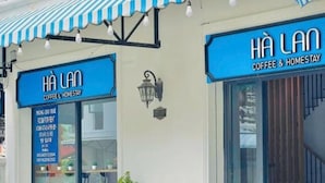 Fachada de una tienda con toldo azul y letrero que dice 'HA LAN COFFEE & HOMESTAY'.