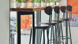 Una casa de huéspedes con café y vistas a un edificio a través de la ventana. Hay plantas en macetas en el alféizar y una mesa con sillas al frente.