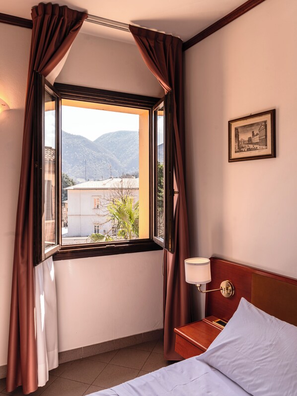 A hotel room with a bed, a nightstand, a lamp, a framed picture on the wall, and a window with curtains. - Misa Hotel (Marzabotto)