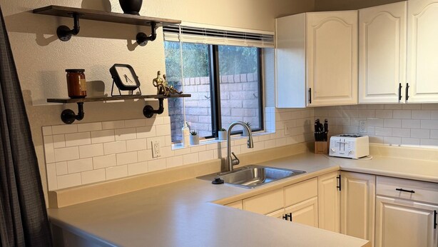 A modern kitchen with white cabinetry, a built-in sink, a stainless steel trash bin, and a window with a view of the outside. - SUMMER TIME SPECIALS!
Enjoyable 2-bedroom condo with AC in vibrant Tempe. (Tempe)