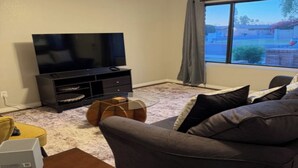 A living room with a flat-screen TV, a sofa, a coffee table, and a window with a view of a residential area. - SUMMER TIME SPECIALS!
Enjoyable 2-bedroom condo with AC in vibrant Tempe. (Tempe)