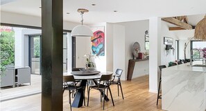 A modern kitchen with a marble countertop, a dining area with a round table and chairs, and a large window providing a view of greenery outside. - Luxurious Villa Chiberta • Pool • 5 suites • Golf & Beach (Anglet)