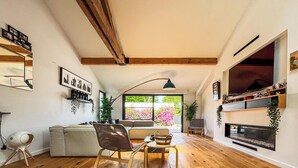 Uma sala de estar com sofá, poltrona, mesa, lareira e uma grande janela com vista para o verde.