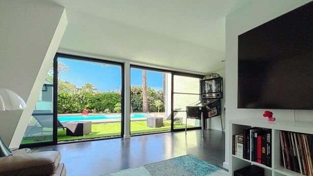 Uma sala de estar moderna com uma grande porta de vidro que dá para uma piscina, uma estante de livros e uma televisão de tela plana.
