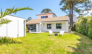 A two-story house with a tiled roof, a small patio with two chairs, and a well-maintained lawn. - Luxurious Villa Chiberta • Pool • 5 suites • Golf & Beach (Anglet)