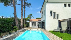 Uma casa moderna com piscina, deck de madeira e um jardim com árvores.