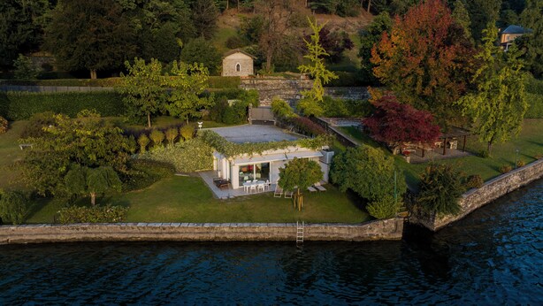 Una casa con un muro in pietra, un piccolo giardino e vista sull'acqua.