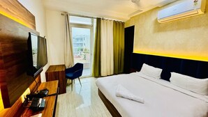 A hotel room with a bed, a desk with a TV, a chair, and an air conditioning unit. - Palette Convention Hotel Millennium (Gurugram)
