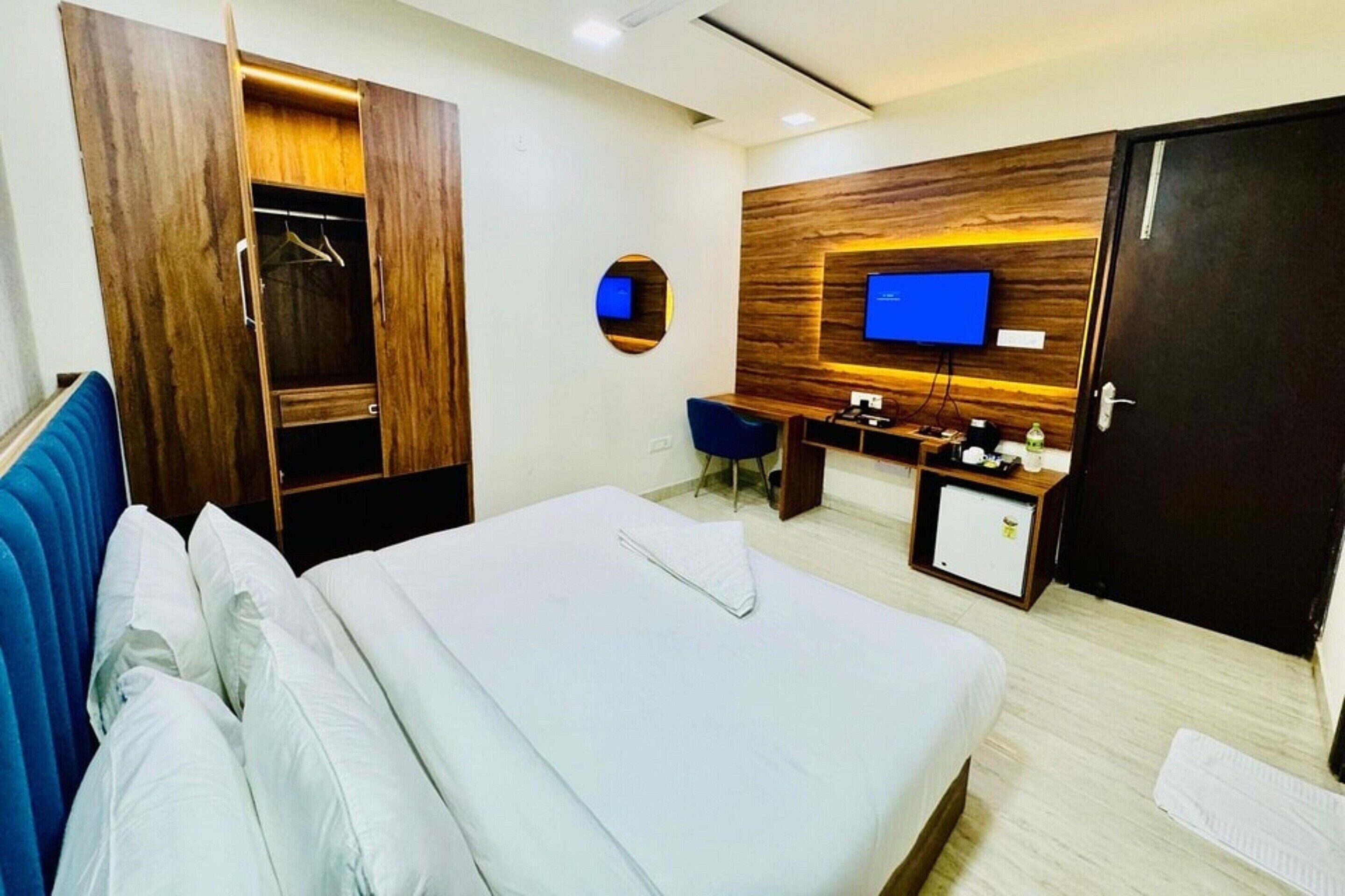 Una habitación de hotel con cama, armario, escritorio, televisor y un refrigerador pequeño.