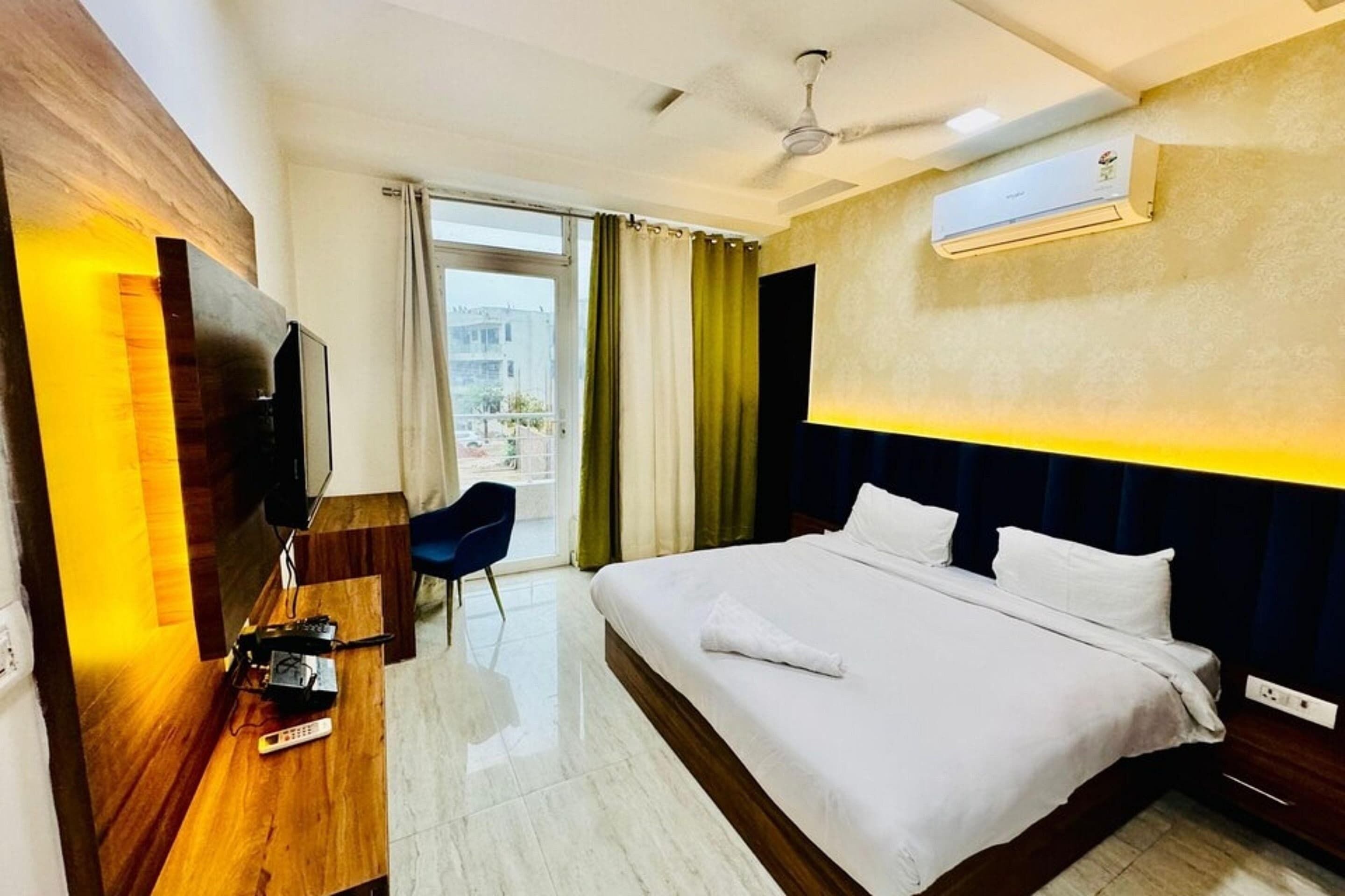 A hotel room with a bed, a desk with a TV, a ceiling fan, and an air conditioning unit.