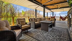 Une terrasse extérieure aménagée avec des meubles en osier, un ventilateur de plafond et une vue sur les arbres et les montagnes.