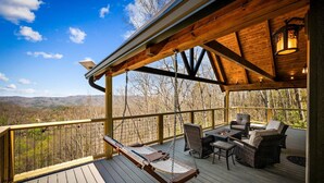 Une terrasse en bois avec une balançoire, des meubles en osier et un foyer.