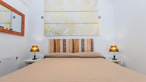 Een hotelkamer met een bed, twee bedlampen, een grote spiegel en een kunstwerk aan de muur.