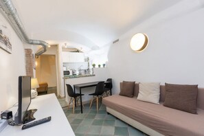 Ein kompakter Wohnbereich mit Sofa, Esstisch mit Stühlen, Fernseher und Küchenzeile.