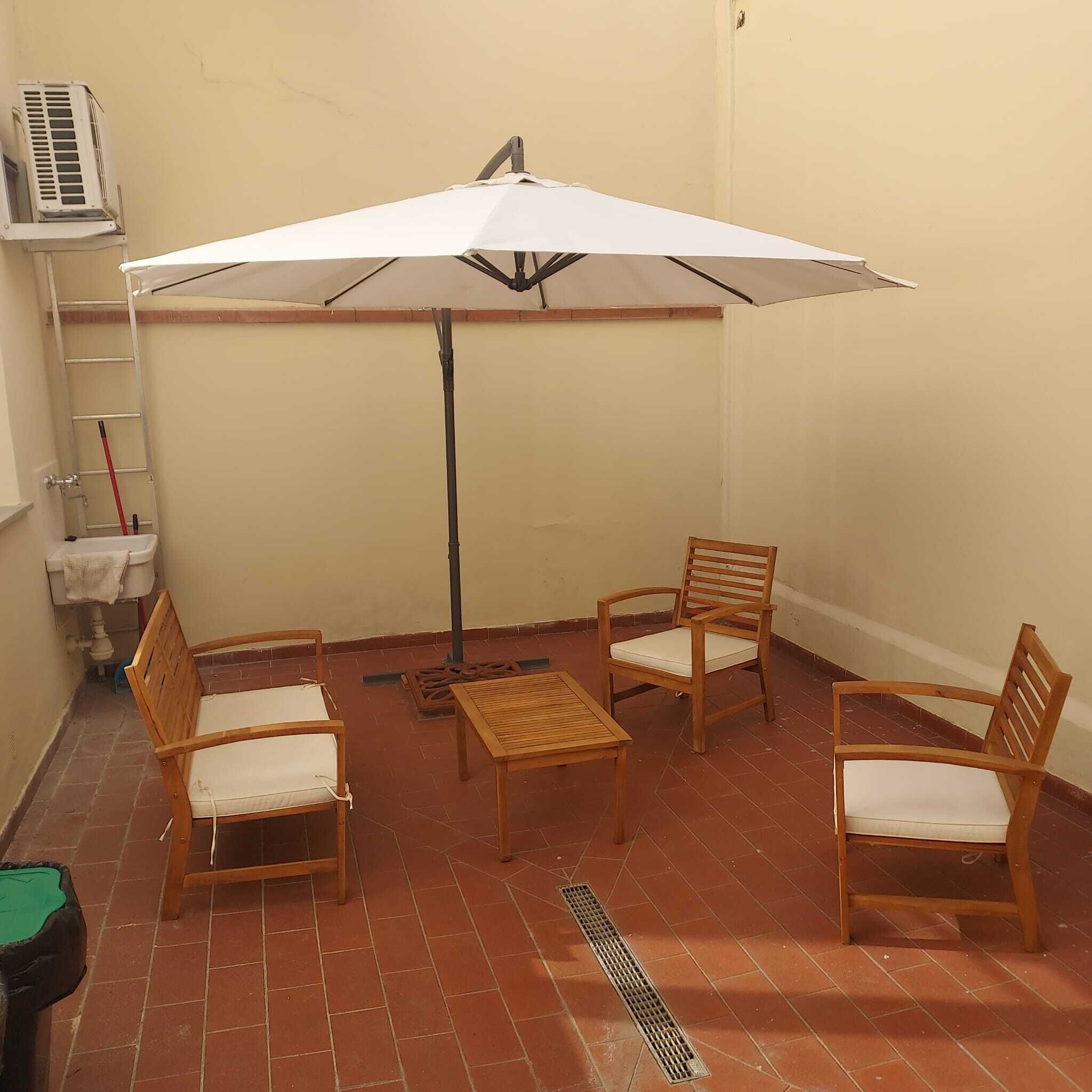 Un piccolo patio con tavolo e quattro sedie, un ombrellone bianco e una scala appoggiata al muro.