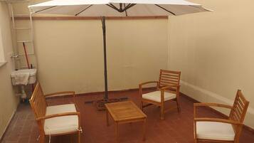 Un piccolo patio con tavolo e quattro sedie, un ombrellone bianco e una scala appoggiata al muro.
