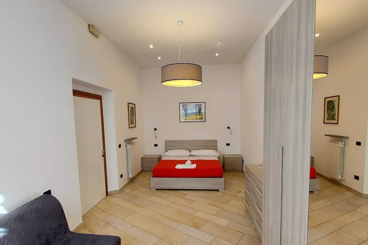 Un dormitorio con una cama, una mesita de noche, una lámpara colgante y una puerta.