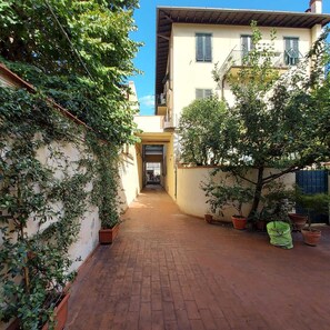 A narrow alleyway with a building on the right, potted plants, and a clear sky. - Amalia Apartments - Via la Farina (Florence)