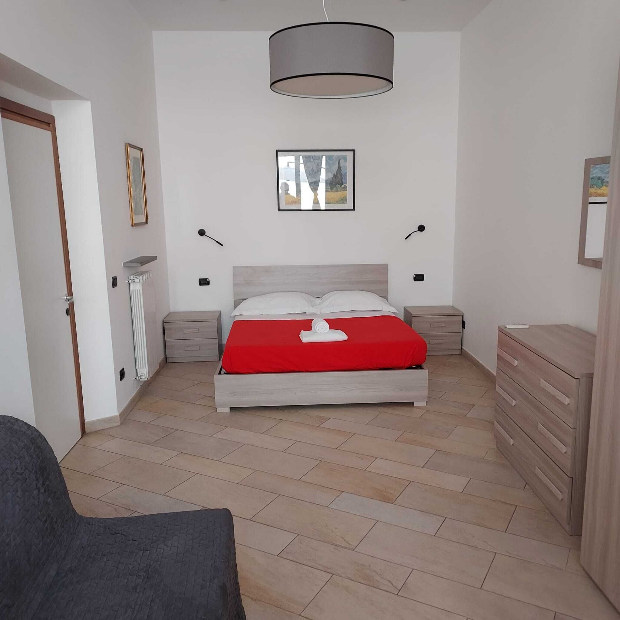 A bedroom with a bed, bedside tables, a dresser, a radiator, a door, and a framed picture on the wall.