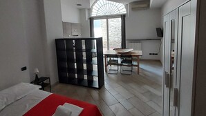 Een slaapkamer met een bed, een rode accentmuur, een zithoek met een tafel en stoelen, en een keuken met een raam en kastjes.