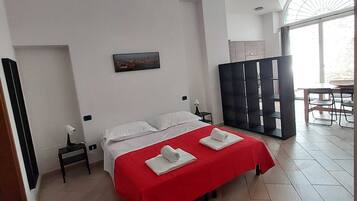 Habitación de hotel con cama, mesita de noche, lámpara, un cuadro, zona de comedor y un gran ventanal.