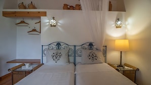 Un letto matrimoniale con cuscini decorativi, un comodino, una lampada e un cestino appeso.