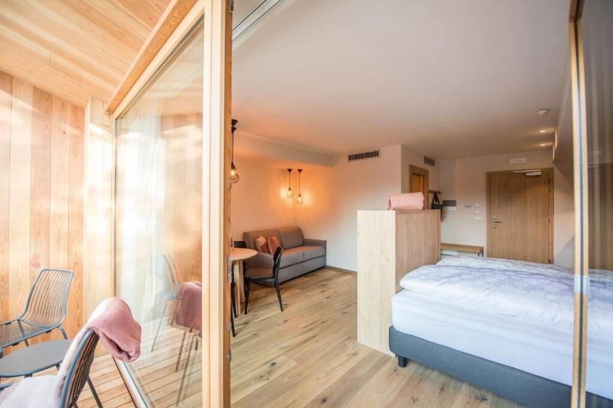 A modern room with a bed, a sofa, a dining table, and chairs.